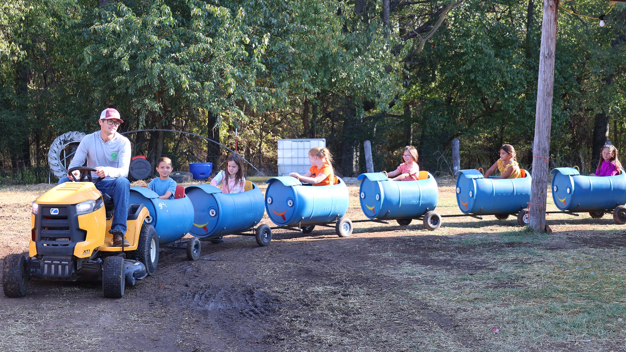 Kids on a train made of water barrels pulled by a riding lawnmower. 